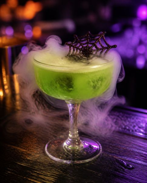Smoking green Halloween cocktail with a spider web garnish